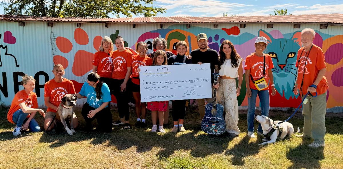 Randy Rogers and family present a donation check with humane society staff, volunteers, and dogs